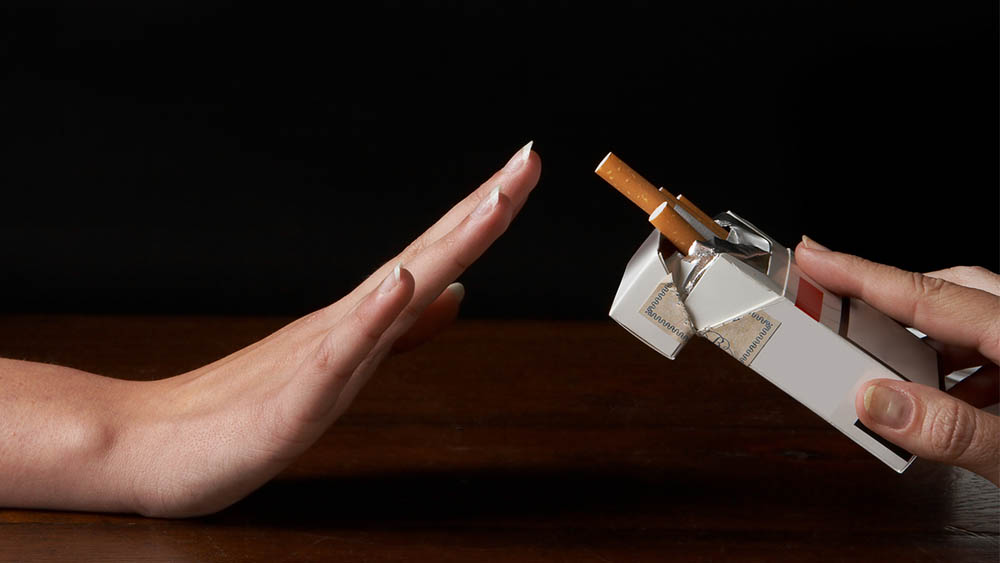 Mão sinalizando "não" para outra mão que oferece uma caixa de cigarros.