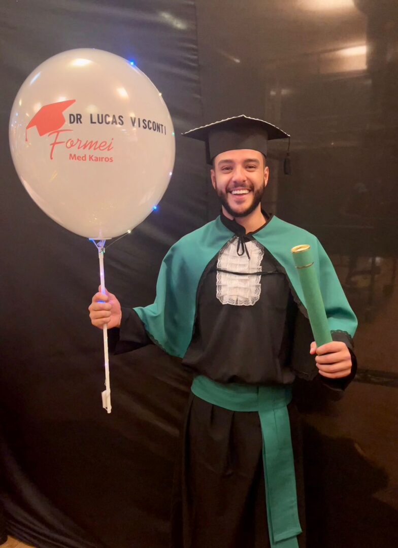Foto mostra Lucas Visconti em sua formatura segurando um balão e o  canudo de formatura.